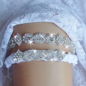 May include: A white satin garter with two rows of sparkling rhinestone embellishments. The garter is decorated with a delicate, intricate design.