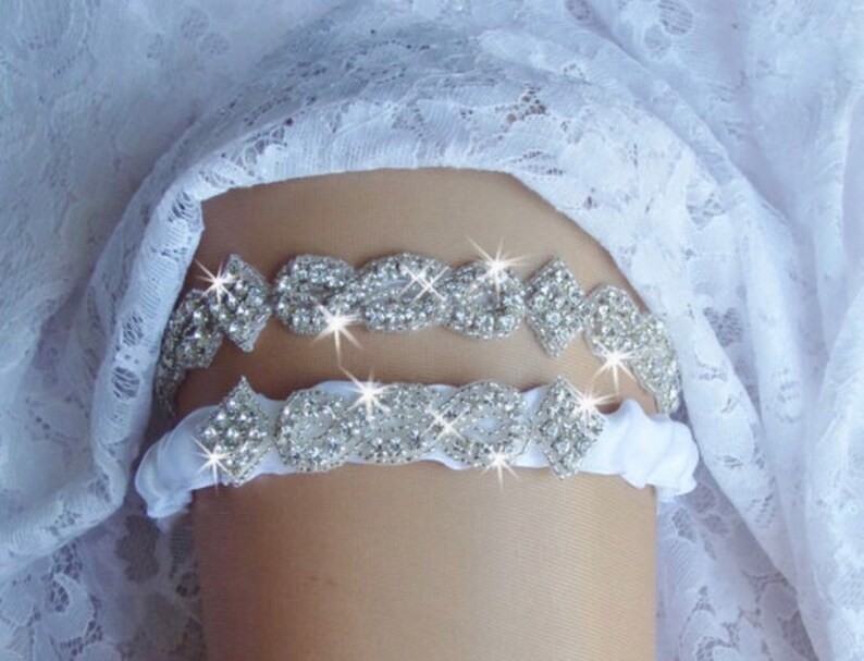 May include: A white satin garter with two rows of sparkling rhinestone embellishments. The garter is decorated with a delicate, intricate design.