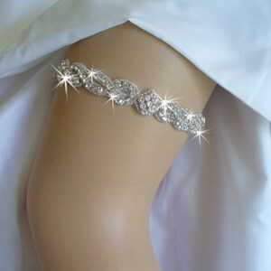 May include: A silver rhinestone garter with a delicate, intricate design. The garter is made of a flexible band with a row of sparkling rhinestones.