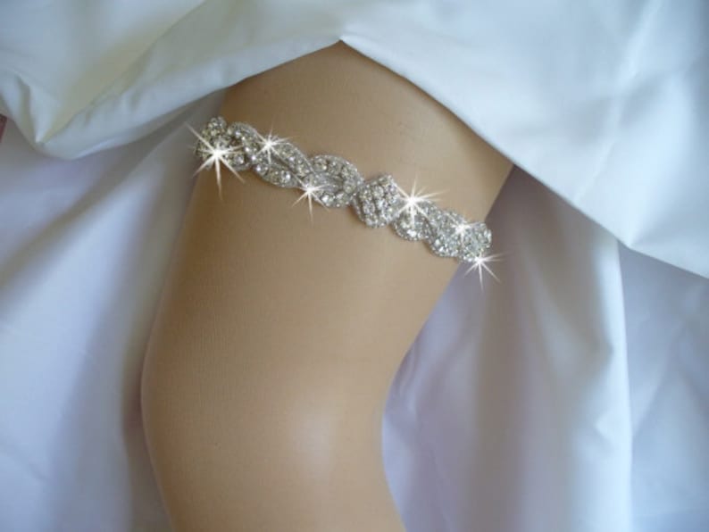 May include: A silver rhinestone garter with a delicate, intricate design. The garter is made of a flexible band with a row of sparkling rhinestones.
