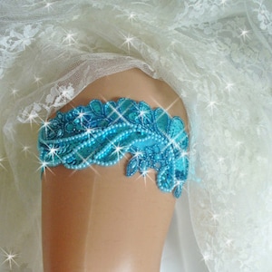 Puede incluir: Una liga de novia azul turquesa con adornos de cuentas y un delicado dise&ntilde;o de encaje.