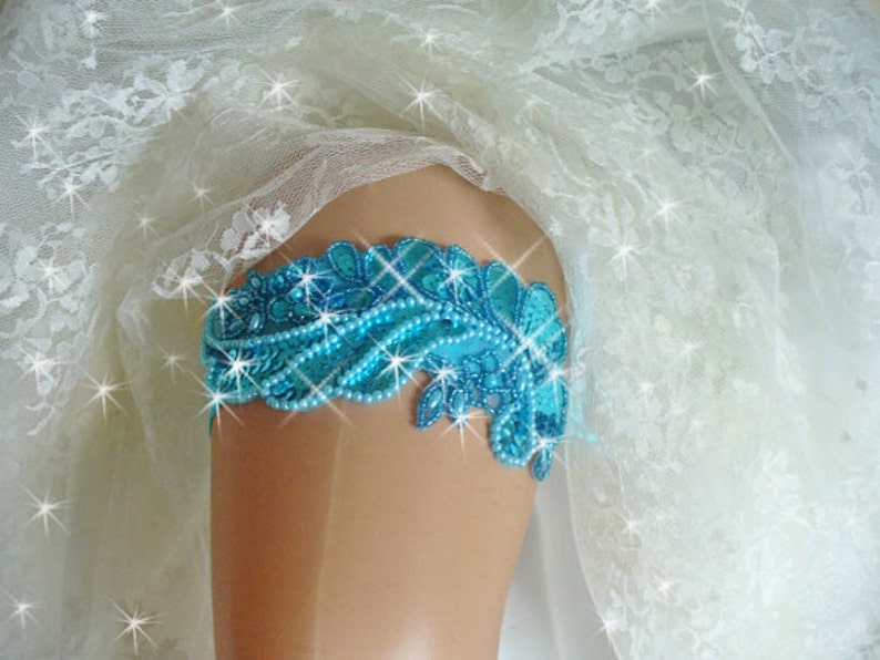Puede incluir: Una liga de novia azul turquesa con adornos de cuentas y un delicado dise&ntilde;o de encaje.
