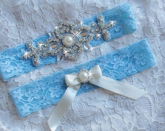 Pode incluir: Uma liga de noiva azul claro com um laço de cetim branco e um grande enfeite de strass. O enfeite apresenta uma pérola no centro.