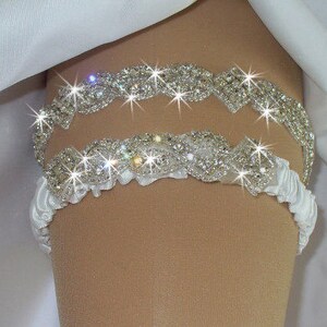 May include: A white satin garter with two rows of silver rhinestone embellishments. The garter is decorated with a delicate ruffle.