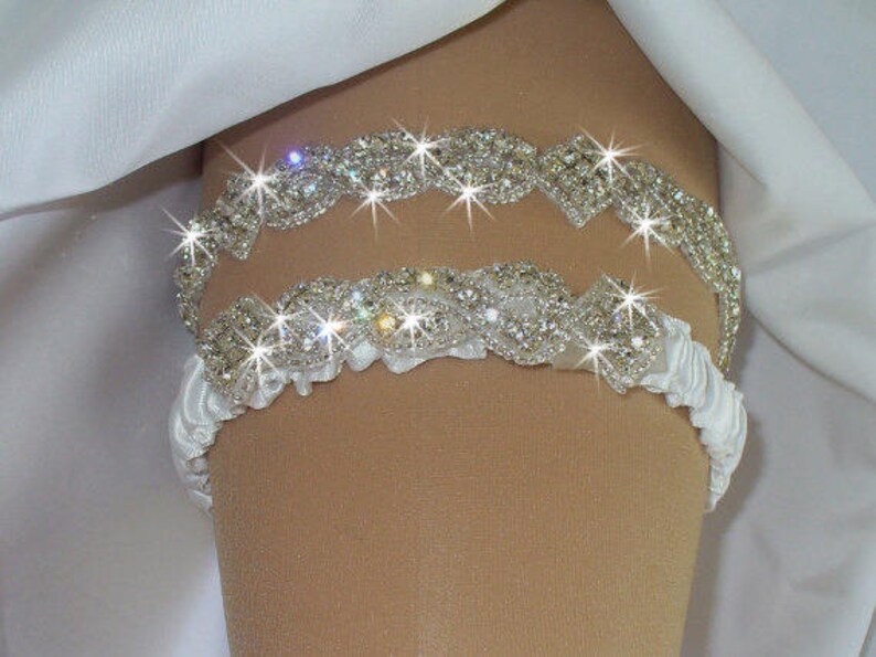 May include: A white satin garter with two rows of silver rhinestone embellishments. The garter is decorated with a delicate ruffle.