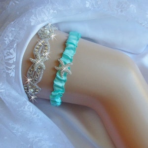 K&ouml;nnte beinhalten: Ein t&uuml;rkisblaues Satin-Strumpfband mit einem Strass-Seestern-Anh&auml;nger. Das Strumpfband liegt auf einem wei&szlig;en Spitzenhintergrund.