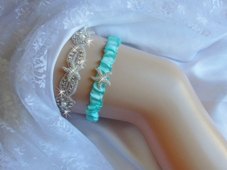 K&ouml;nnte beinhalten: Ein t&uuml;rkisblaues Satin-Strumpfband mit einem Strass-Seestern-Anh&auml;nger. Das Strumpfband liegt auf einem wei&szlig;en Spitzenhintergrund.