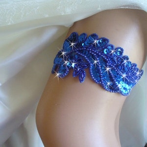 Puede incluir: Una liga azul real con un dise&ntilde;o floral de cuentas y lentejuelas. La liga est&aacute; adornada con brillantes pedrer&iacute;as.