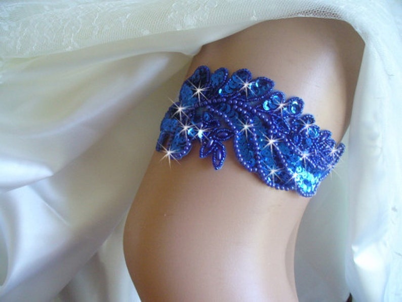 Puede incluir: Una liga azul real con un dise&ntilde;o floral de cuentas y lentejuelas. La liga est&aacute; adornada con brillantes pedrer&iacute;as.