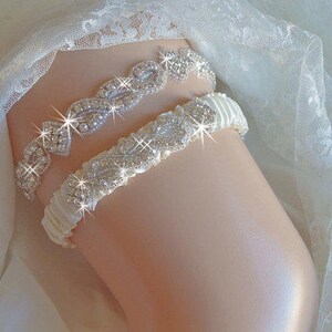 May include: A white satin garter with a crystal rhinestone embellishment. The garter is decorated with a delicate floral design.