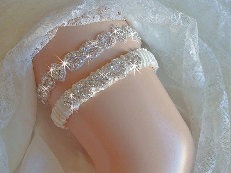 May include: A white satin garter with a crystal rhinestone embellishment. The garter is decorated with a delicate floral design.