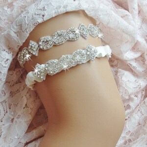 May include: Two white satin garters with rhinestone embellishments. The garters are decorated with rows of sparkling rhinestones.