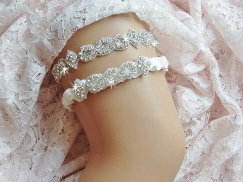 May include: Two white satin garters with rhinestone embellishments. The garters are decorated with rows of sparkling rhinestones.