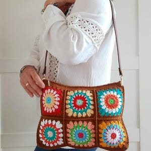 May include: A brown crochet shoulder bag with colorful floral squares. The bag features a long brown strap and a zipper closure. The squares are in shades of red, orange, yellow, green, and blue.
