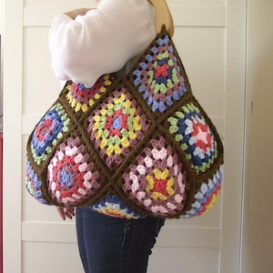 May include: A colourful, handmade crochet bag with a patchwork design. The bag is made up of granny squares in pink, blue, yellow, and green, with brown yarn outlines. It has a wooden handle.