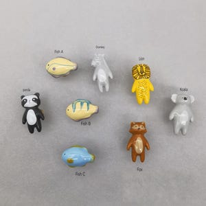 Puede incluir: Conjunto de diez tiradores de cajones de cerámica con diferentes diseños de animales, incluyendo un panda, un pez, un burro, un león, un koala y un zorro. Los tiradores están pintados en colores brillantes y tienen un estilo caprichoso.