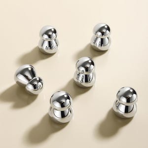 Op de afbeelding: Zes zilverkleurige, ronde, decoratieve knoppen met een gladde, glanzende afwerking. De knoppen hebben een paddenstoelvorm met een afgeronde bovenkant en een iets bredere basis.