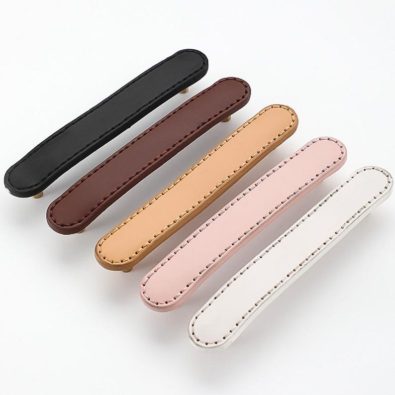 May include: Six leather drawer pulls in various colours, including black, brown, beige, pink, and white. Each pull has a stitched edge and a gold metal screw.
