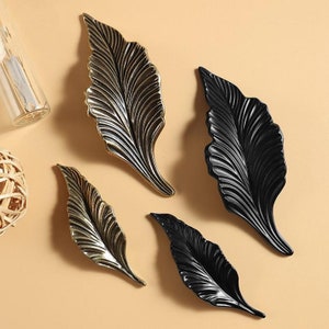 May include: Four decorative leaf-shaped cabinet pulls in two finishes: gold and black. The pulls have a detailed, textured design.