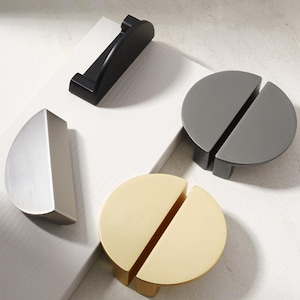 May include: Four cabinet door pulls in different finishes: brushed nickel, black, gold, and gray. Each pull is a half-circle shape with a split in the middle.