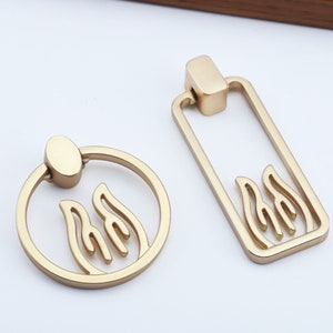 May include: Two gold-toned cabinet pulls with a flame design. One pull is a ring with a round knob, the other is a rectangular pull with a rounded top.