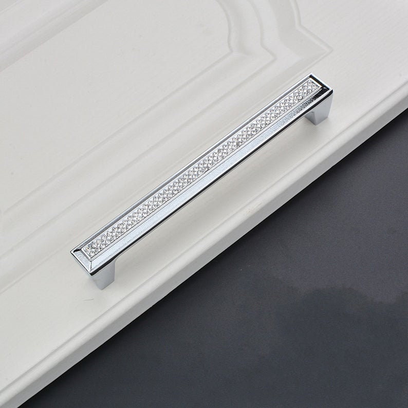 May include: A silver cabinet door handle with a row of clear rhinestones.