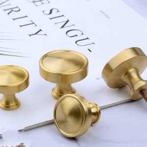 Può includere: Tre pomelli per armadi in ottone con una parte superiore rotonda leggermente bombata e una base cilindrica. I pomelli sono lucidati a una finitura lucida.