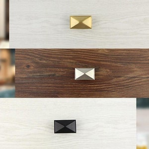 Puede incluir: Tres pomos de armario en diferentes acabados: dorado, plateado y negro. Cada pomo es una forma geom&eacute;trica con una parte superior e inferior puntiagudas.