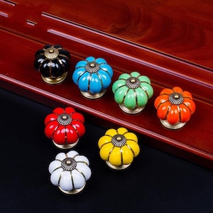 Peut inclure: Ensemble de huit boutons de porte en céramique en forme de citrouille dans différentes couleurs, notamment noir, bleu, vert, orange, rouge, blanc et jaune. Chaque bouton a une base en métal doré.