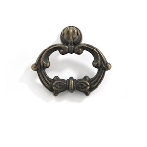 Peut inclure: Une poignée de tiroir ovale ornée avec un motif de nœud décoratif. La poignée est en métal et a une finition bronze foncé.