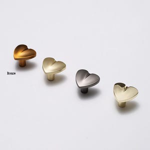 Könnte beinhalten: Vier herzförmige Schrankknöpfe in verschiedenen Ausführungen: Bronze, Gold, Silber und Schwarz.