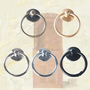 Può includere: Set di cinque tiretti ad anello in metallo di diversi colori. I tiretti sono rotondi con un piccolo pomo nella parte superiore. I tiretti sono in argento, oro, nero e due tonalità di bronzo.