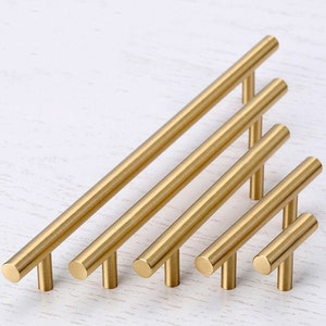 Puede incluir: Conjunto de seis tiradores de armario de color dorado en varios tamaños. Los tiradores tienen un diseño simple y moderno con una barra recta y una manija en forma de T.