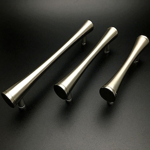 May include: Three brushed nickel cabinet pulls of varying lengths. The pulls are cylindrical with a slight taper at each end.