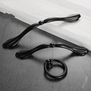 以下が含まれることがあります： 装飾的な曲線デザインの黒い金属製のキャビネットプルが3つあります。プルはサイズが異なり、最大のプルは約30cmの長さです。