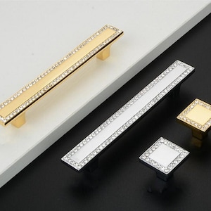 Op de afbeelding: Drie kastknoppen met een diamantvormig ontwerp. De knoppen zijn gemaakt van metaal en hebben een glanzende afwerking. De knoppen zijn verkrijgbaar in goud en zilver.