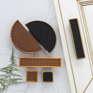 May include: Assortment of cabinet hardware pulls in a woven pattern. The pulls are in gold and black finishes. The pulls are in various shapes, including round, square, and rectangular.