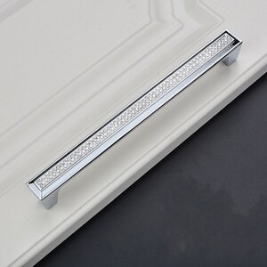 May include: A silver cabinet door handle with a row of clear rhinestones.