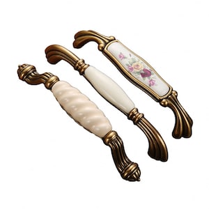 May include: Three decorative cabinet pulls with brass-colored metal bases. The center pull has a smooth, white ceramic handle. The other two pulls have textured, white ceramic handles, one with a floral design. These pulls are ideal for adding a touch of elegance to furniture.