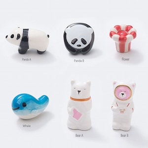 Könnte beinhalten: Set mit 6 Essstäbchenablagen aus Keramik mit verschiedenen Tier- und Blumenmotiven. Das Set enthält einen Panda, einen Wal, eine Blume und zwei Bären. Die Essstäbchenablagen sind weiß mit schwarzen, blauen, rosa und roten Akzenten.