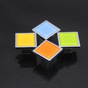 May include: Four square cabinet knobs with a chrome finish and colorful glass inserts. The knobs are blue, yellow, green, and orange.