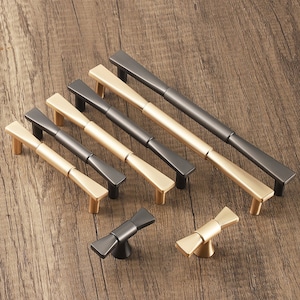 Pode incluir: Um conjunto de seis puxadores de armário em ouro e preto com um design moderno e minimalista. Os puxadores são feitos de metal e têm uma forma retangular elegante. O conjunto também inclui dois puxadores decorativos menores com forma de gravata borboleta.