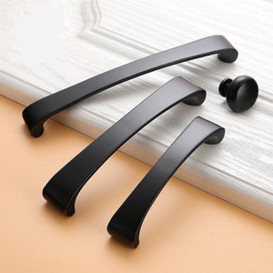 May include: Three black metal cabinet pulls in different sizes. The pulls have a curved shape and a smooth finish.