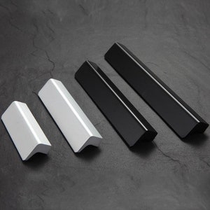 Op de afbeelding: Vier kastgrepen, twee zwart en twee wit, met een gebogen, hoekig ontwerp. De grepen zijn gemaakt van metaal en hebben een gladde afwerking.