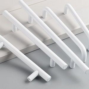 May include: Five white metal cabinet pulls in various styles. The pulls are all made of metal and have a smooth, polished finish.