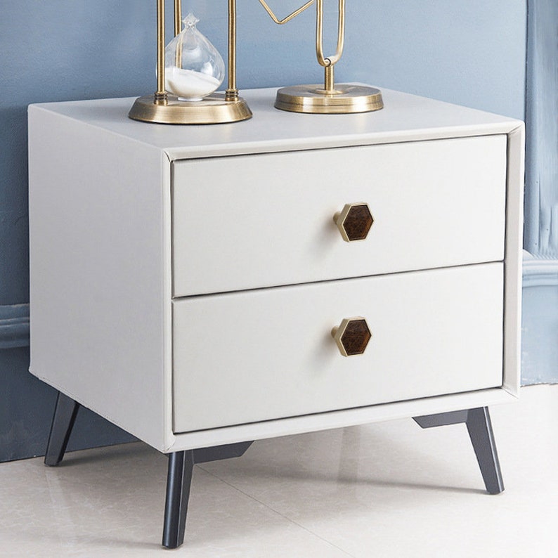 Pu&ograve; includere: Comodino bianco a due cassetti con gambe nere e maniglie dei cassetti esagonali in ottone. Il comodino ha un design moderno ed &egrave; perfetto per una camera da letto.