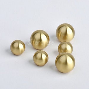 May include: A set of six gold-toned round cabinet knobs. The knobs are different sizes, with the largest being about 1 inch in diameter.