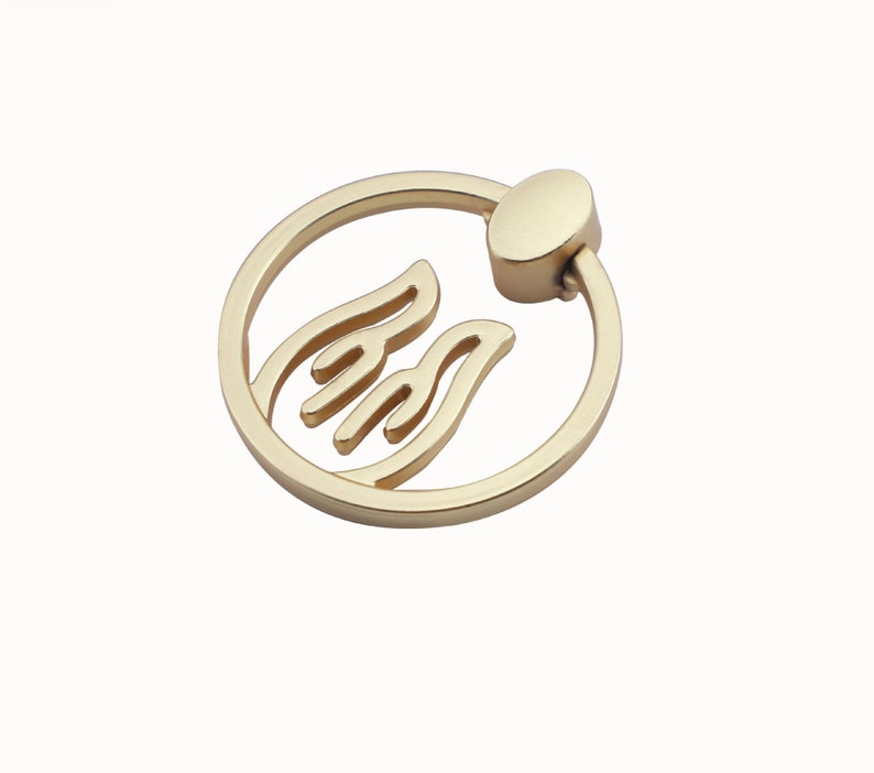 May include: Gold-toned round cabinet pull with a stylized flame design. The pull has a circular ring and a small knob on the side.