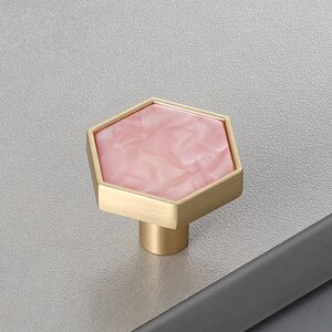 Pu&ograve; includere: Un pomello esagonale per armadio con intarsio in marmo rosa e base in metallo dorato.