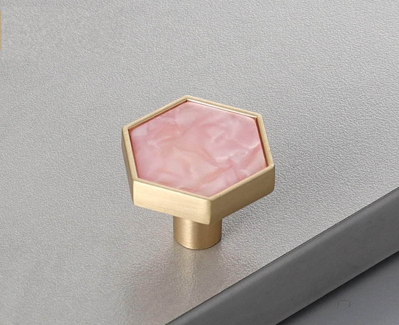 Pu&ograve; includere: Un pomello esagonale per armadio con intarsio in marmo rosa e base in metallo dorato.